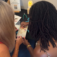 Two women sitting together, one holding a small tray with earrings on it.