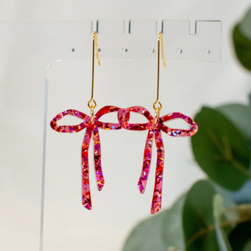 A pair of sparkling pink/red glitter bow earrings, perfect for adding a playful and romantic touch to any outfit.