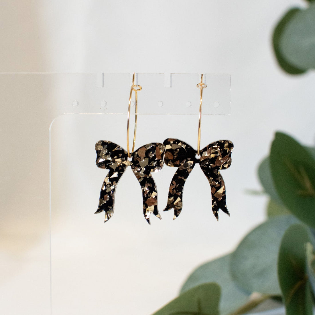 A pair of elegant black and gold glitter bow earrings, perfect for adding sophistication to any outfit.